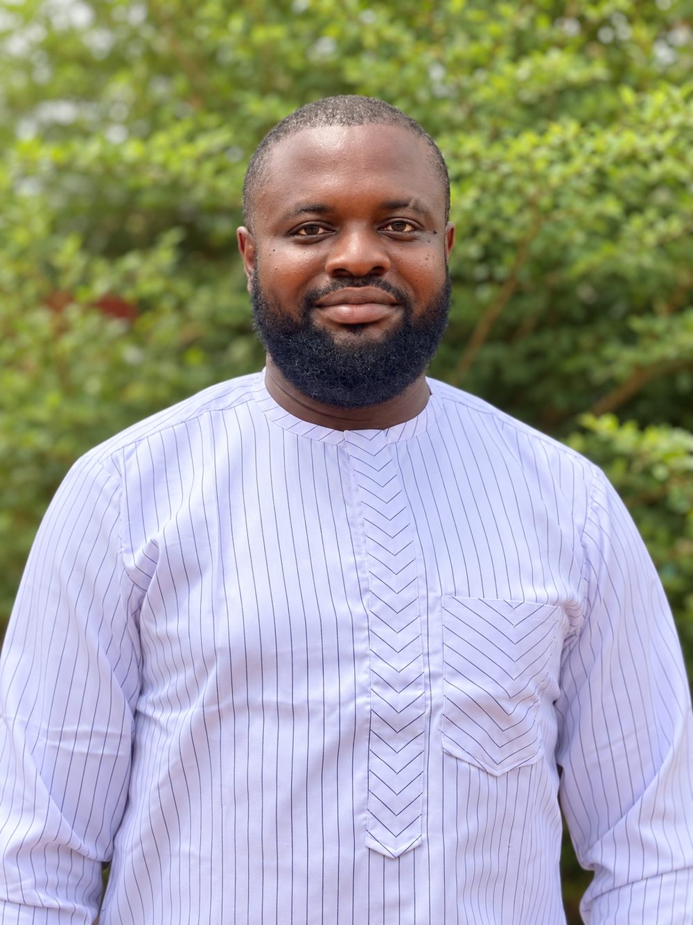 Femi Fragile smiling outdoors in a white striped kaftan